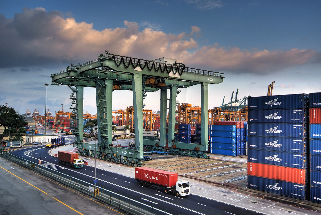 Container cranes, stacked shipping containers and trucks at a Singapore port terminal.